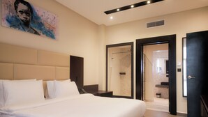Ein modernes Hotelzimmer mit einem großen Bett, einem Gemälde an der Wand, einer Duschkabine und einer Tür zum Badezimmer.