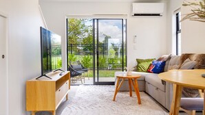 Un salon moderne comprenant un canapé, une table basse, un téléviseur posé sur un meuble en bois et une porte-fenêtre coulissante donnant sur un jardin.