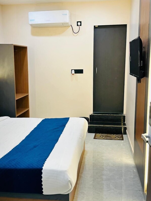 A hotel room with a bed, a wardrobe, a television, and a door. - Hotel grs palace (Varanasi)