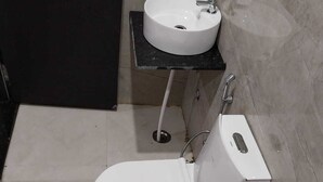 Un baño pequeño y compacto con un inodoro blanco, un lavabo blanco sobre una encimera negra y una puerta negra.