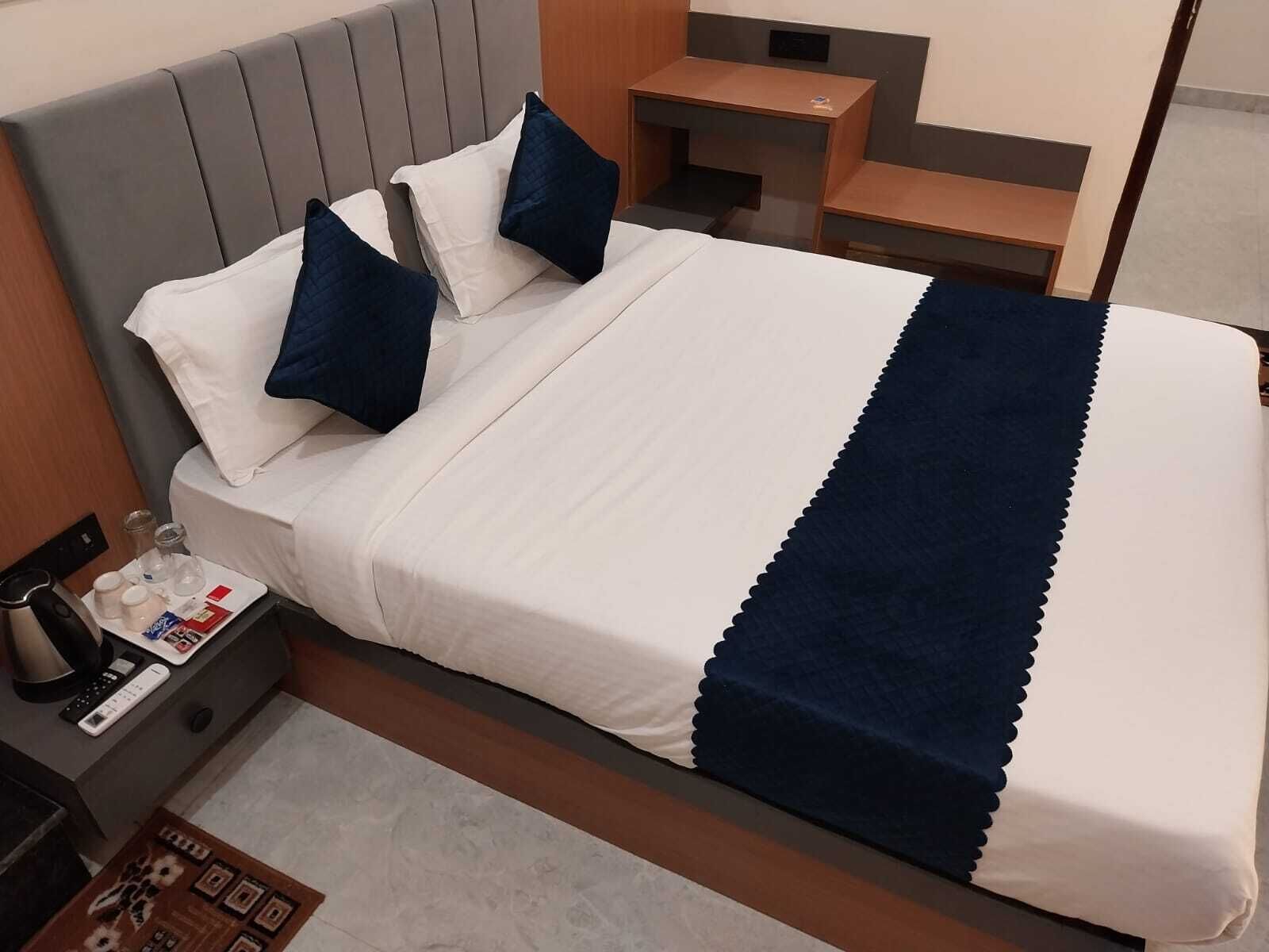Habitación de hotel con cama, una mesita de noche con control remoto, un atril con cafetera y una alfombra pequeña.
