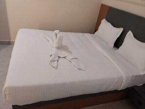 A neatly made bed with white linens and pillows, a wooden headboard, and a plain wall in the background. - Hotel grs palace (Varanasi)