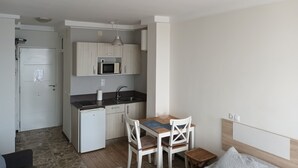 Eine kompakte Küche mit Mikrowelle, Spüle und kleinem Kühlschrank. Es gibt einen Essbereich mit Tisch und Stühlen.
