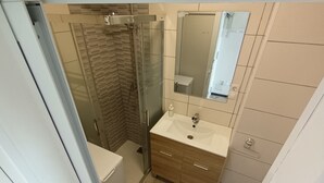 Ein modernes Badezimmer mit einer Duschkabine aus Glas, einem Waschbecken mit Spiegel darüber und Holzschränken.