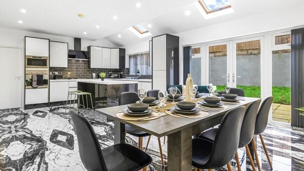 A modern kitchen with a dining area, featuring a large island, black chairs, and a marble floor.