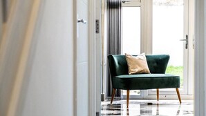 A green armchair with a beige pillow in a hallway with a glass door leading outside.