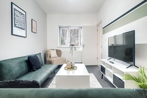 Ein modernes Wohnzimmer mit einem grünen Sofa, einem weißen Couchtisch und einem großen Flachbildfernseher.