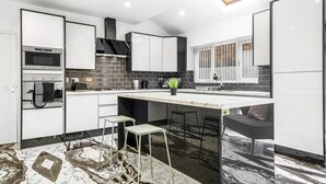 A modern kitchen with white cabinets, a built-in oven, a gas stove, and a large island with stools.