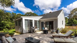 Una casa con patio, mobiliario exterior, una parrilla y una habitación con paredes de vidrio.