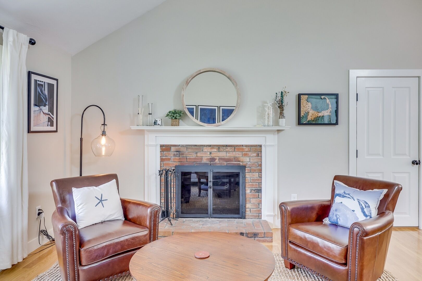 A living room with a fireplace, two leather armchairs, a round coffee table, and a mirror above the fireplace.