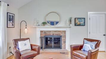 A living room with a fireplace, two leather armchairs, a round coffee table, and a mirror above the fireplace.
