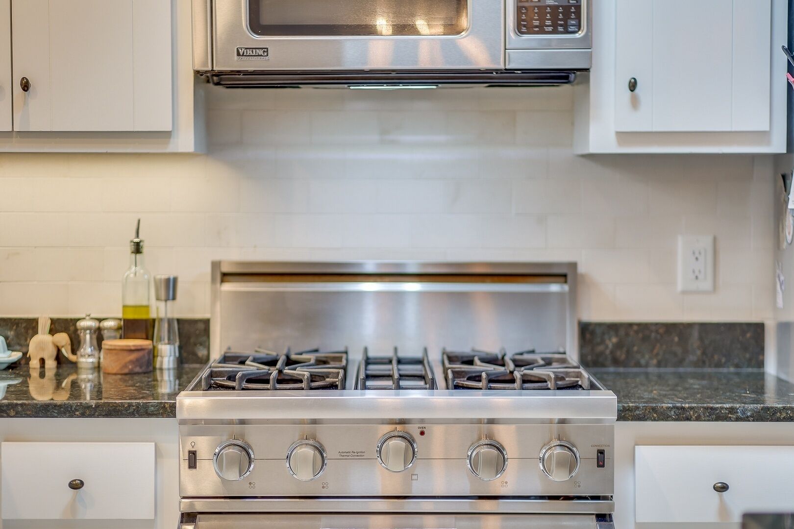 A kitchen with a stainless steel stove, white cabinets, and a microwave above it.