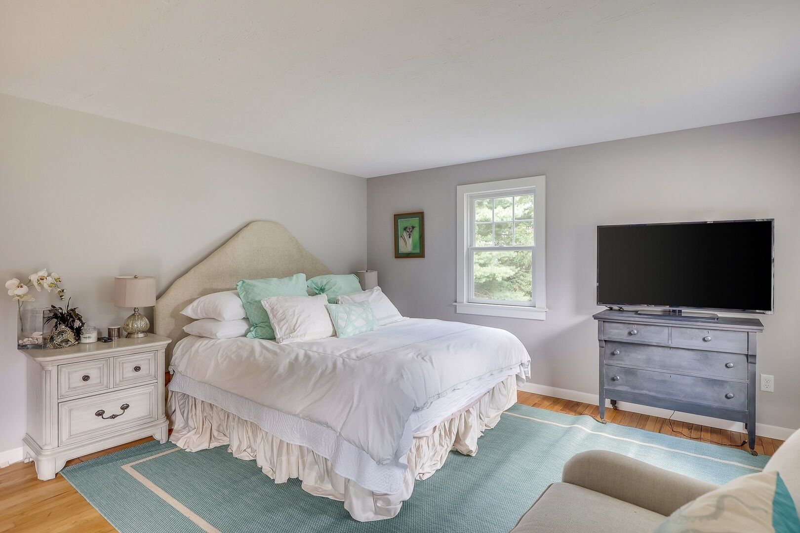 A bedroom with a bed, a dresser, a television, and a window.