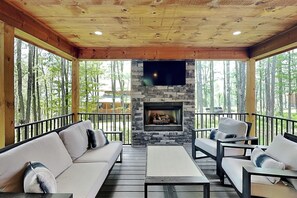 A covered outdoor seating area with a stone fireplace, wooden ceiling, and large windows. - The Pour House by Taylor Made Deep Creek (McHenry)