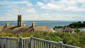 A coastal town with stone buildings, a prominent tower, and a view of the sea.