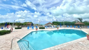 A swimming pool with blue lounge chairs and umbrellas, surrounded by a stone wall and greenery.