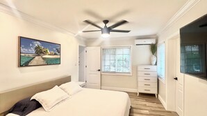 A bedroom with a bed, a ceiling fan, a painting, a dresser, and a window with blinds.