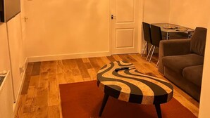 A living room with a wooden floor, a zebra-patterned ottoman, a grey sofa, a chandelier, and a dining table with chairs. - 4 Guests - 10min Airport - N E C - Jaguar (Solihull)