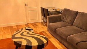 A living room with a grey sofa, a round coffee table with a black and beige pattern, and a wooden floor. - 4 Guests - 10min Airport - N E C - Jaguar (Solihull)