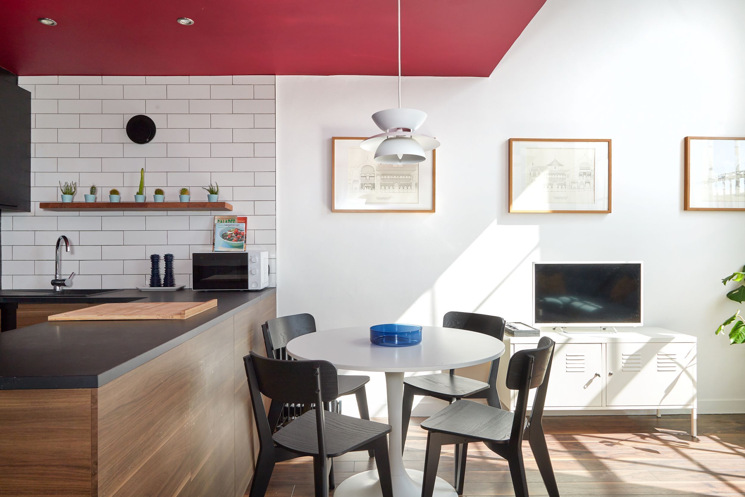 A modern kitchen with a red ceiling, white tiled backsplash, and a wooden countertop. There is a dining area with a round table and four chairs.