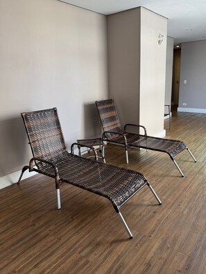 Un pasillo con tres sillones de mimbre alineados junto a una pared, suelo de madera y una puerta al final.