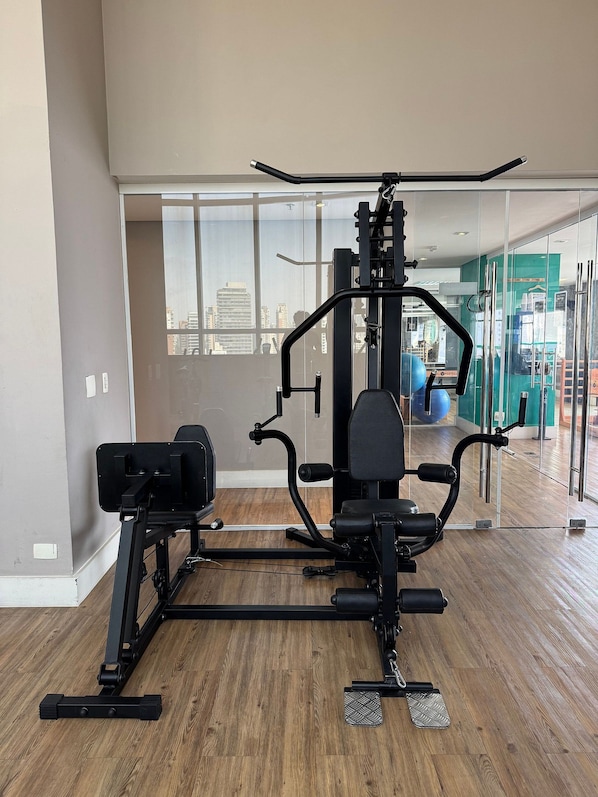 Un gimnasio con equipo de ejercicio, ventanas amplias y vistas a la ciudad.
