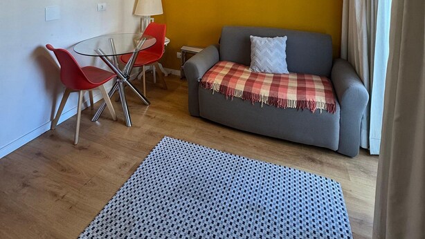 Un pequeño espacio de sala con un sofá, una silla roja, una mesa de vidrio y una lámpara.
