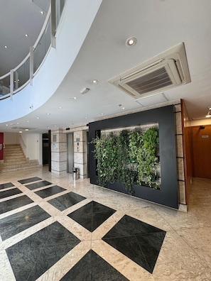 Un moderno vestíbulo con suelo de diseño geométrico, un jardín vertical y una escalera que conduce a un nivel superior.