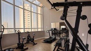 Un gimnasio con equipo de ejercicio, ventanas amplias y vistas a la ciudad.