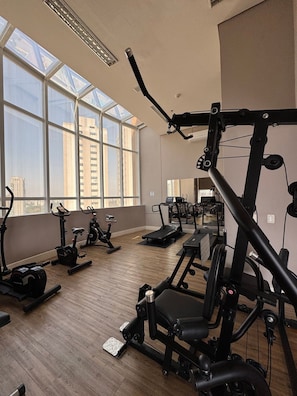 A gym with exercise equipment, large windows, and a city view.