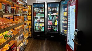 Interior de una tienda con estantes llenos de aperitivos y bebidas, y dos vitrinas refrigeradas.