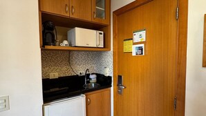 Una cocina compacta con armarios de madera, microondas, cafetera y refrigerador.