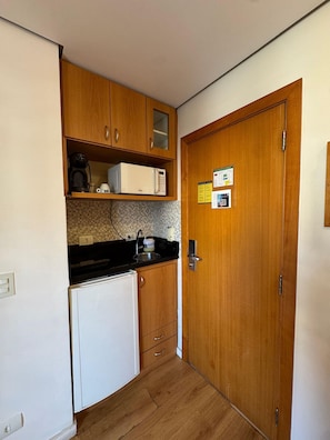 A compact kitchen with wooden cabinets, a microwave, a coffee maker, and a refrigerator. - Get a Flat 601 Ibirapuera -Jardins (São Paulo)