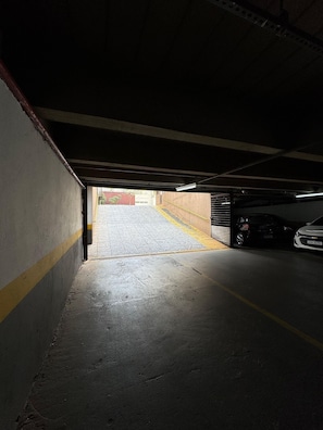 A dimly lit parking garage with a wet floor, a yellow line on the wall, and a car parked in the distance. - Get a Flat 601 Ibirapuera -Jardins (São Paulo)