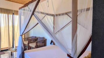 A wooden-framed bed with a canopy, a small wooden table, and a chair in a room with a tiled floor and wooden ceiling.