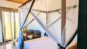 Una habitación con techo de madera, una cama con mosquitera, una mesita pequeña y una silla.