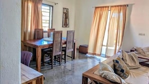 Un espacio de sala con un sofá de madera, una mesa de comedor con sillas y una lámpara colgante.