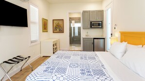 A bedroom with a bed, a bedside table, a chair, a TV, a painting, and a view into the bathroom. - Sorrento Cabana: 1-Bedroom Cabana Near Vanderbilt Beach – Perfect for a Tranquil Beachside Escape (Naples)