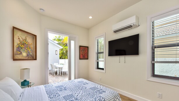 A bedroom with a bed, a TV mounted on the wall, and a window with blinds. - Sorrento Cabana: 1-Bedroom Cabana Near Vanderbilt Beach – Perfect for a Tranquil Beachside Escape (Naples)