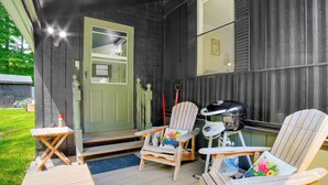 A wooden deck with two Adirondack chairs and a small table, a door, and a window. - Peaceful Brookside Getaway ~10 Mi to Okemo Slopes! (Chester)