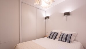 Quarto com cama, almofadas, mesa de cabeceira e luminária na parede.