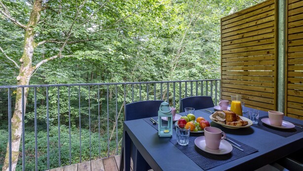 Varanda com mesa posta para o café da manhã, rodeada por vegetação exuberante.