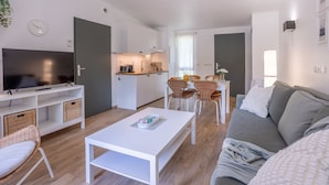 Una sala de estar moderna con un televisor de pantalla plana, una mesa de centro blanca, un sofá gris, sillas de mimbre y una mesa de comedor con sillas.
