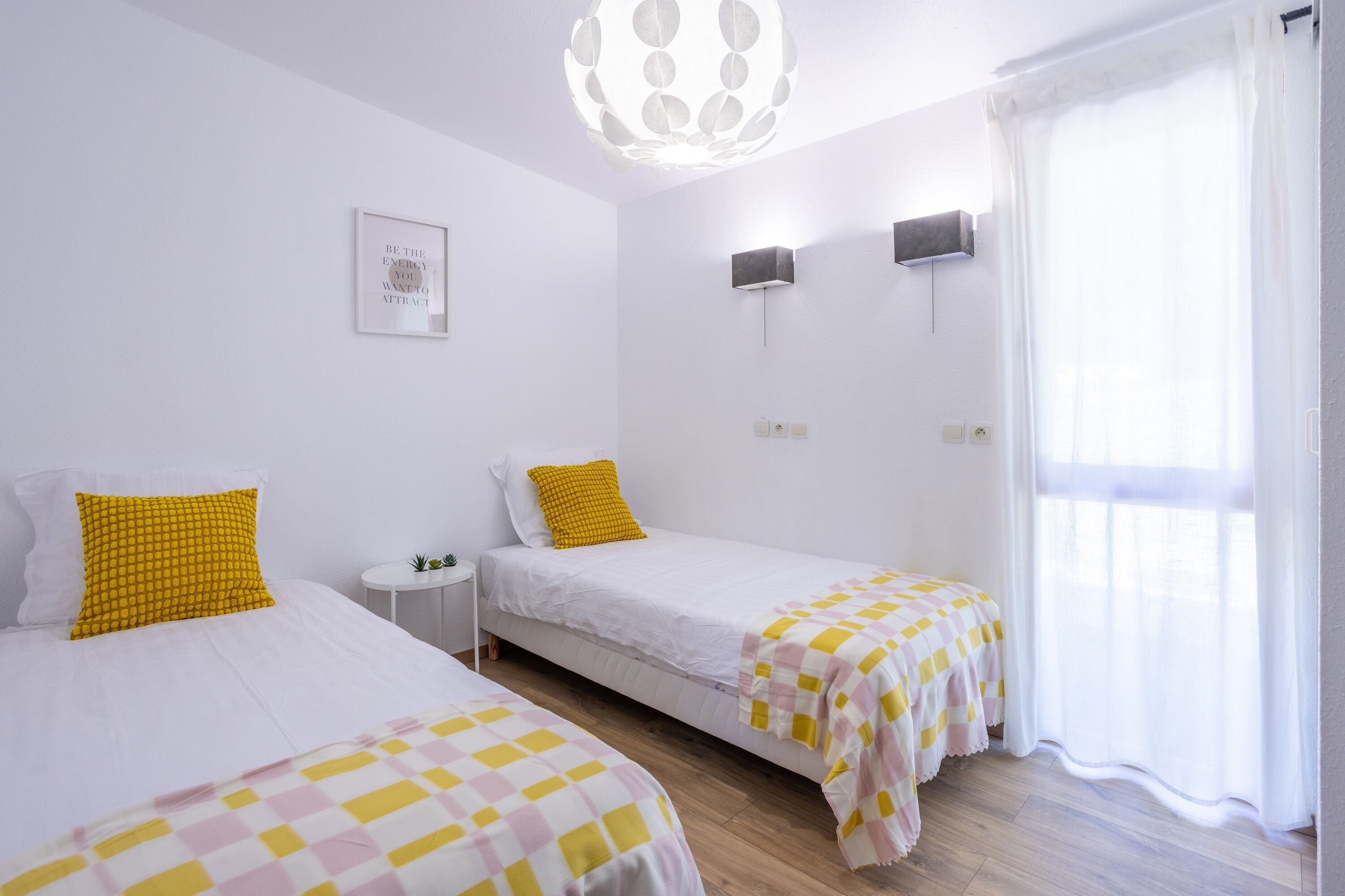 Une chambre avec deux lits, une petite table de chevet, une lampe fixée au mur et une fenêtre avec des rideaux.