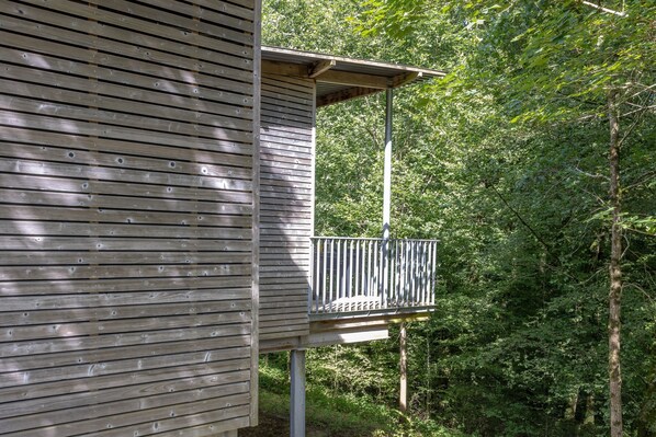 A wooden cabin with a balcony overlooking a forested area.