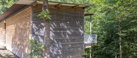 Un piccolo chalet in legno con un balcone, immerso in una fitta foresta.