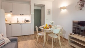 Eine moderne Küche mit weißen Schränken, einem Essbereich mit rundem Tisch und Stühlen, einer Couch und einem Fernseher auf einem Holzständer.