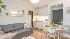 Ein modernes Wohnzimmer mit einem grauen Sofa, einem runden Couchtisch und einem Essbereich mit einem weißen Tisch und Stühlen.