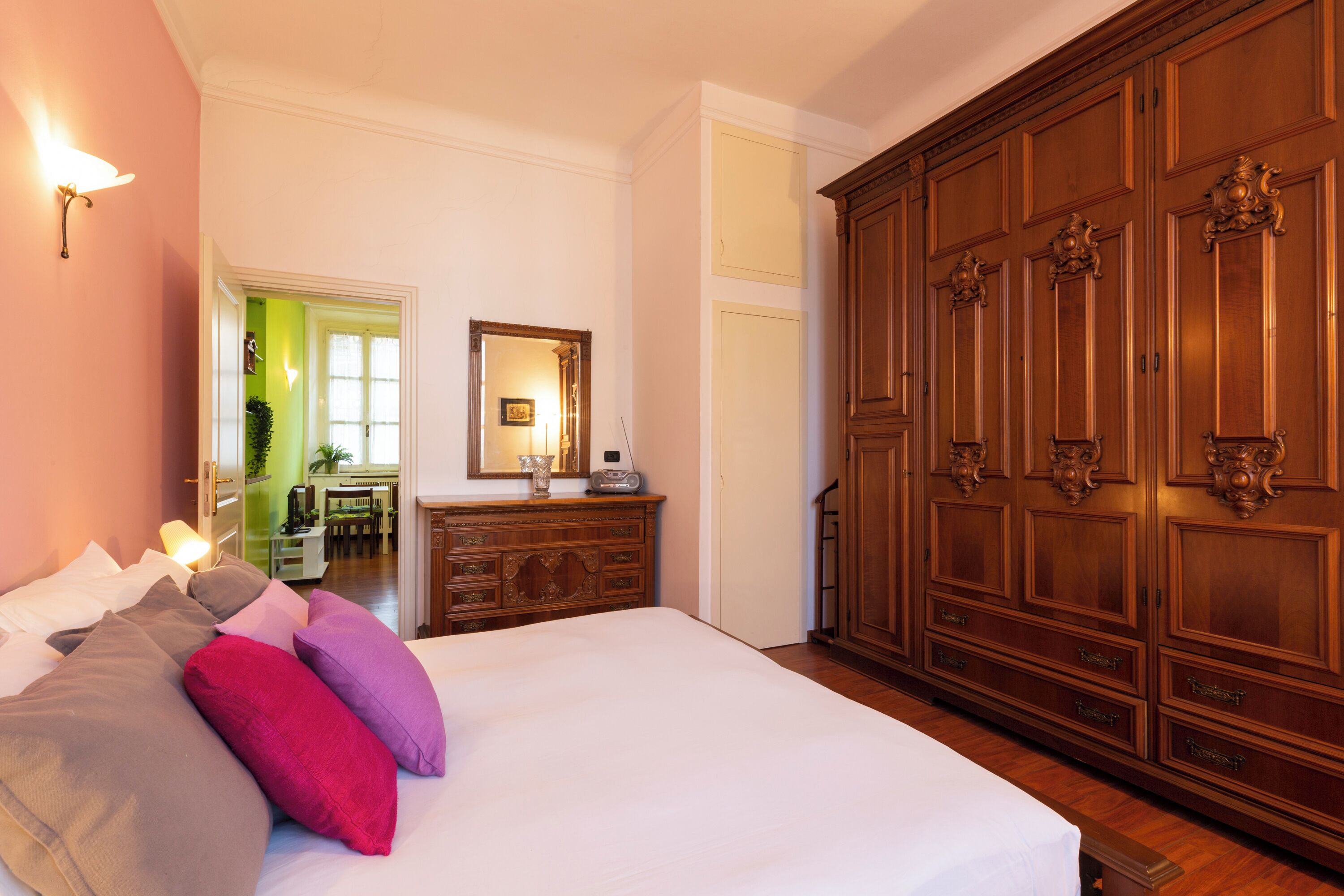 A bedroom with a large bed, a dresser, a mirror, and a wardrobe.