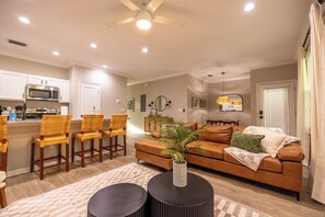 A modern living room with a brown sofa, a coffee table, and a dining area with wicker chairs.